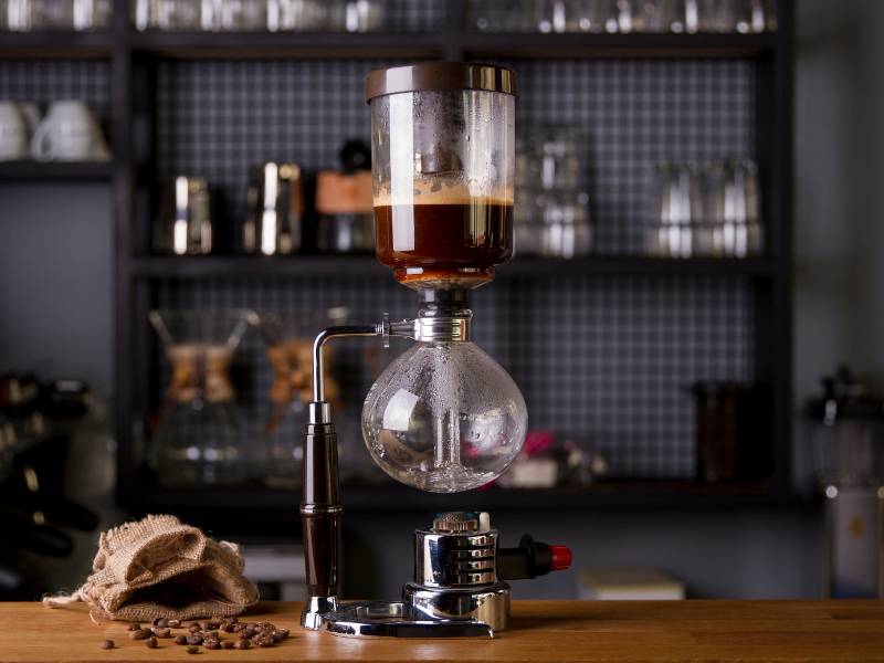 Hario Technica Siphon coffee maker on bench next to open bag of coffee beans