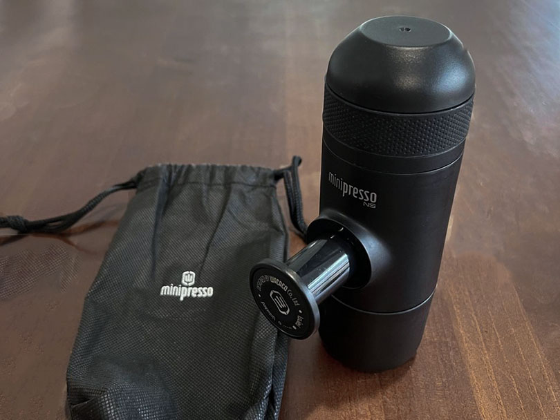 Wacaco Minipresso on table beside drawstring travel bag - manual pump is extended