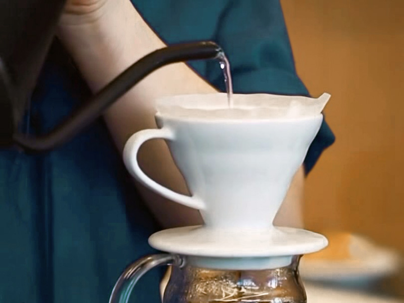 Pouring water from gooseneck kettle into Hario V60 pour over cone (white)