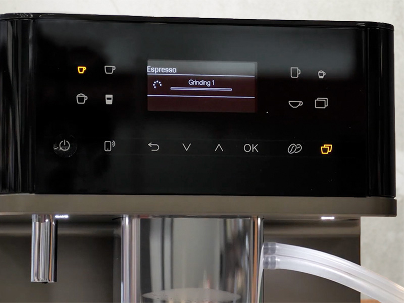 Close-up of the Miele CM 6360 user interface. Screen says 'Espresso Grinding 1', and the 2 x drinks button is lit up