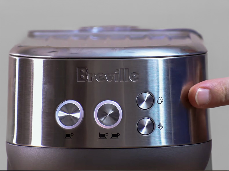Finger pointing to the simple 4 button user interface of the Breville Bambino