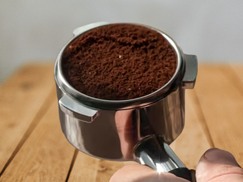 Hand holding the 54mm portafilter for the Breville Bambino, filled with freshly ground coffee