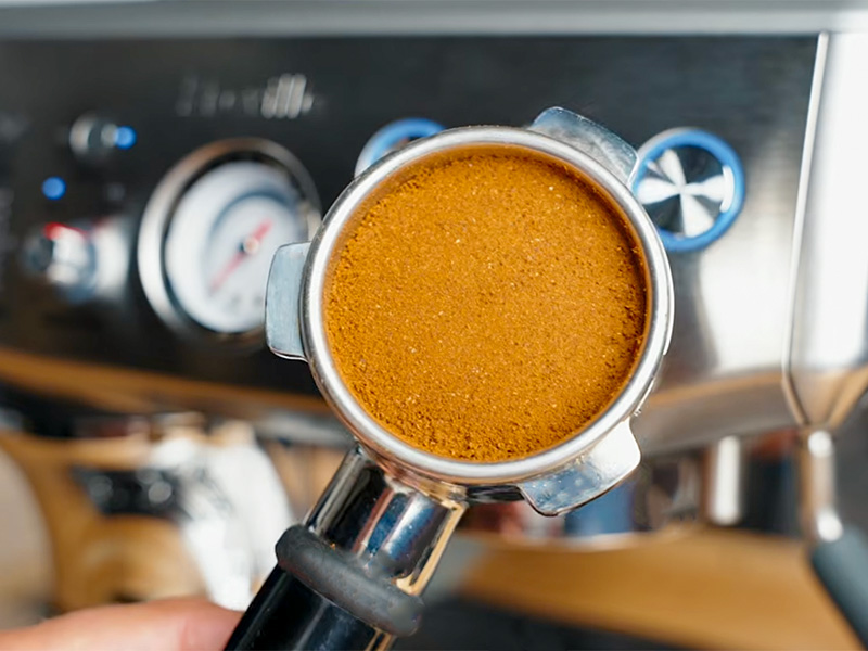 Holding the portafilter with freshly tamped coffee grounds in front of the Breville Barista Express Impress